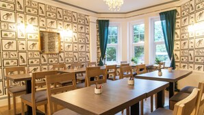 A dining area with wooden tables and chairs, framed animal illustrations on the walls, and a chandelier. - The Cherry Tree B&B Hotel (Eastbourne)