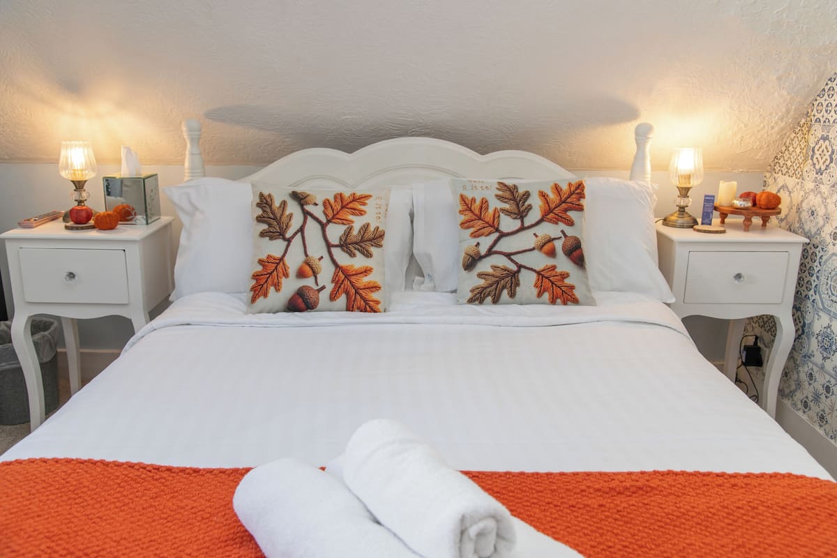 A neatly made bed with white bedding and orange accents, flanked by two nightstands with lamps and decorative items.