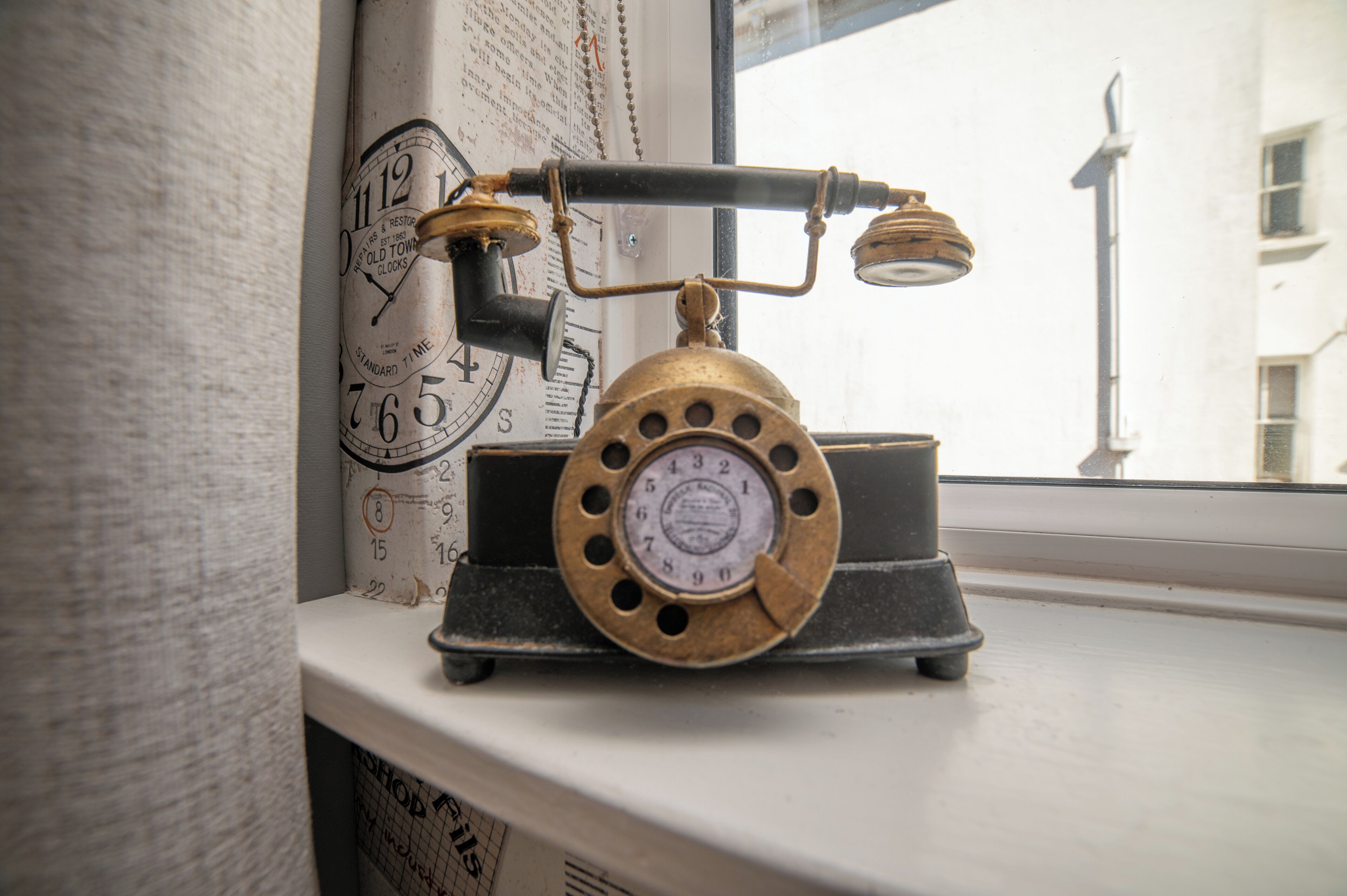 Un vieux téléphone posé sur un rebord de fenêtre, d’où l’on aperçoit une rue et des bâtiments.