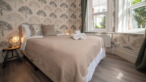 A neatly made bed with a beige blanket, a bedside lamp, and a rolled towel on the bed. - The Cherry Tree B&B Hotel (Eastbourne)
