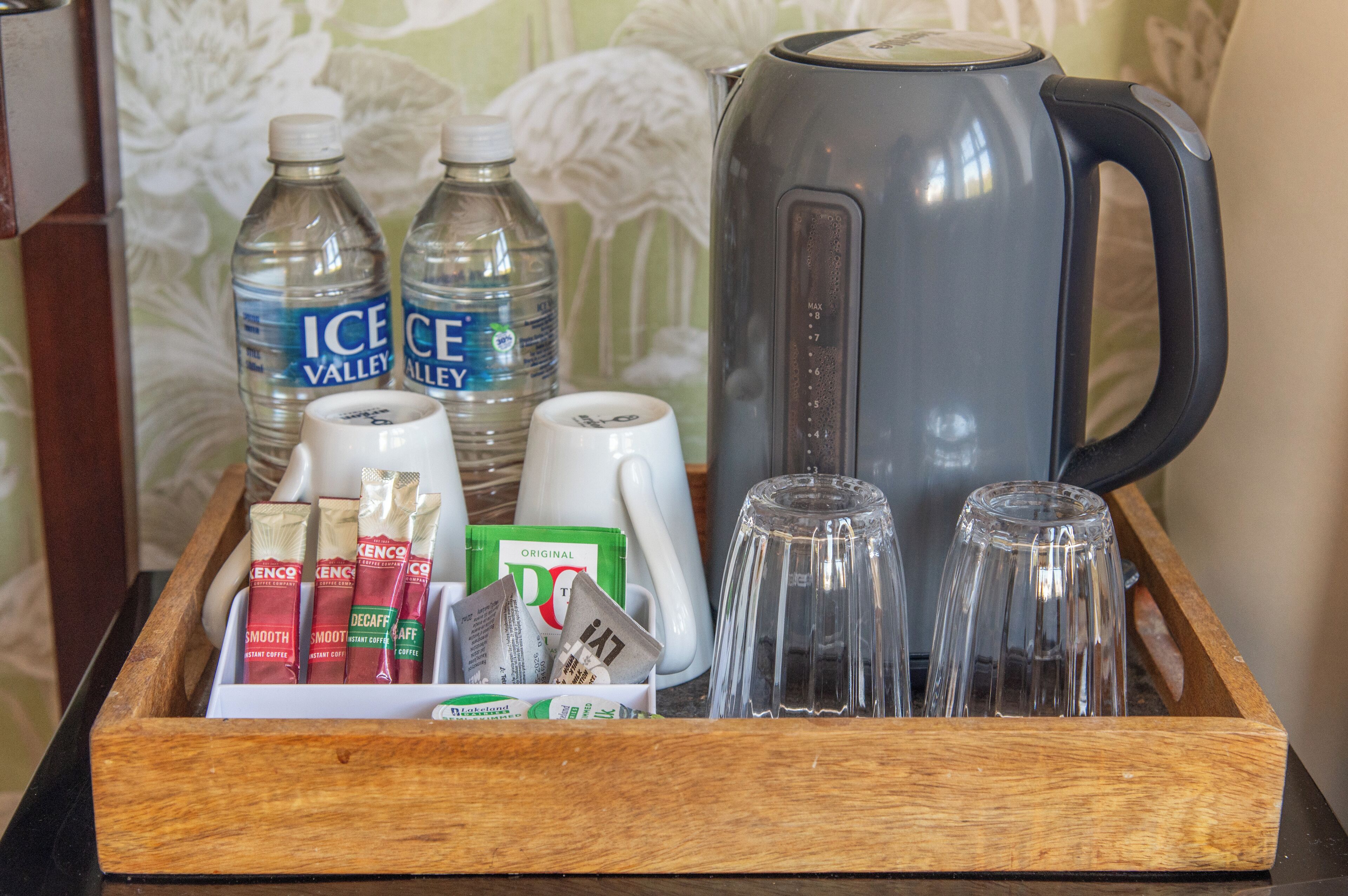 A tray with coffee pods, tea bags, bottled water, a kettle, and glassware.