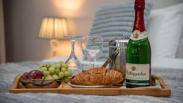 A tray with a bottle of Rölkäppchen, grapes, a croissant, and glasses on a bed.