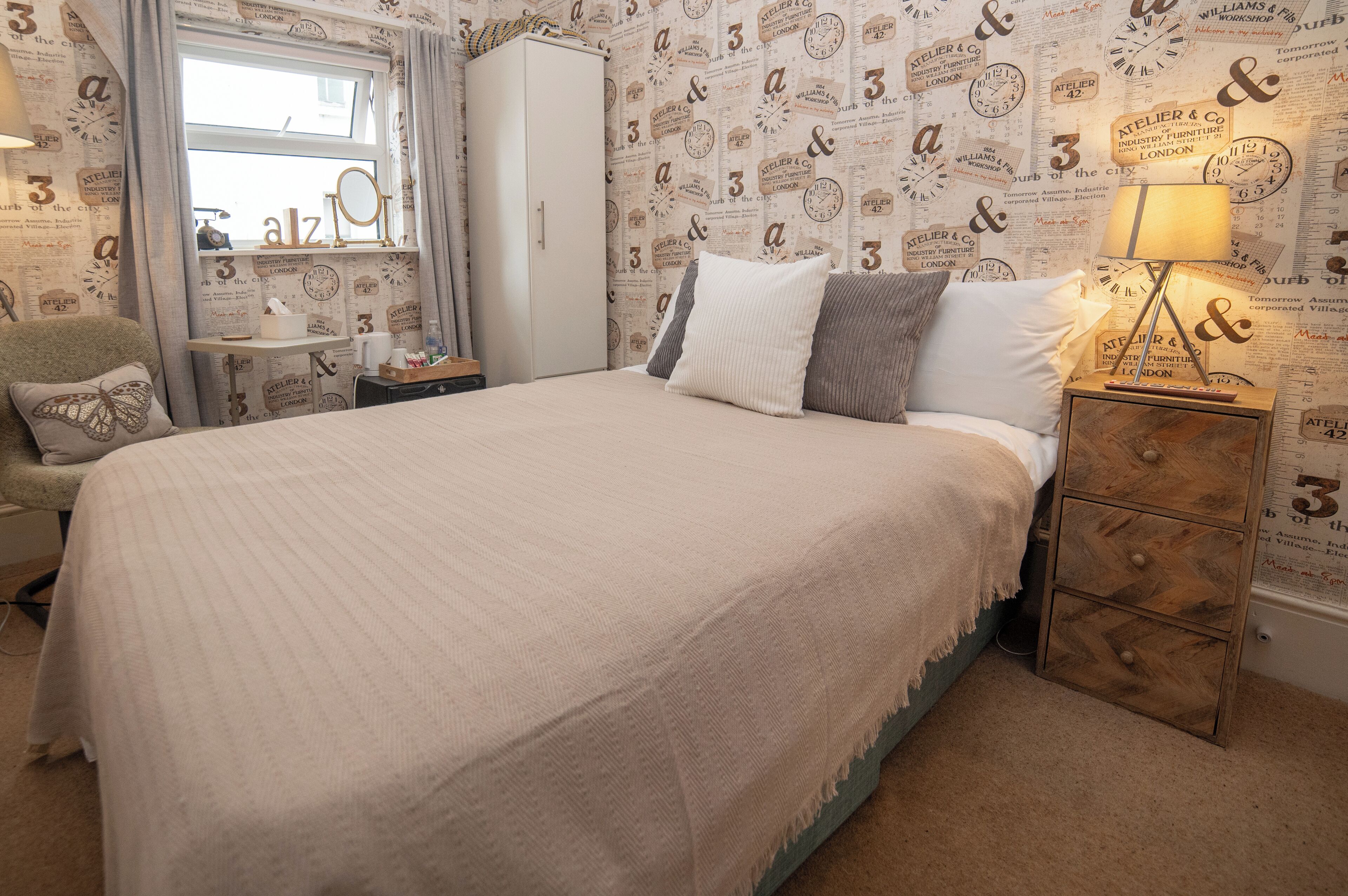 A bedroom with a large bed, a bedside table with a lamp, a wardrobe, and a window with curtains.