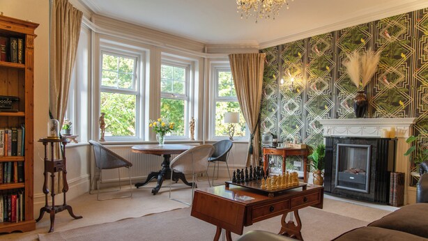 A living room with a fireplace, a chessboard, a bookshelf, and a window with curtains. - The Cherry Tree B&B Hotel (Eastbourne)