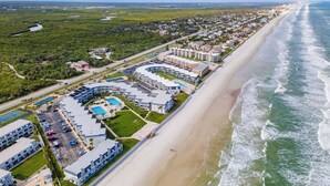 Un hôtel situé sur la côte, composé de plusieurs bâtiments, doté d’une longue plage et d’une piscine.
