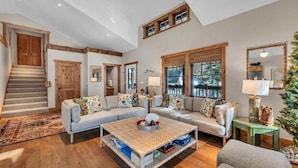 A spacious living room with a large sectional sofa, a coffee table, and a staircase leading to an upper level. - Camp Carnelian |  Walk to Lake Tahoe + Quiet Deck (Carnelian Bay)