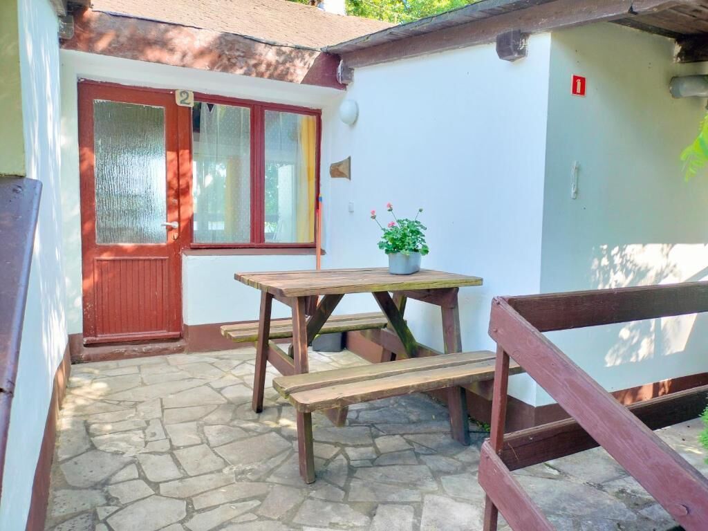 A small outdoor area with a wooden table and benches, a red door, and a potted plant.