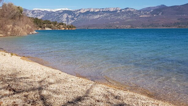 A clear view of a lake with a pebbly shore and mountains in the background.