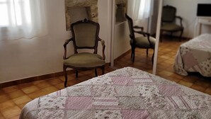 A bedroom with a wooden floor, a bed with a floral quilt, a chair, and a mirror.