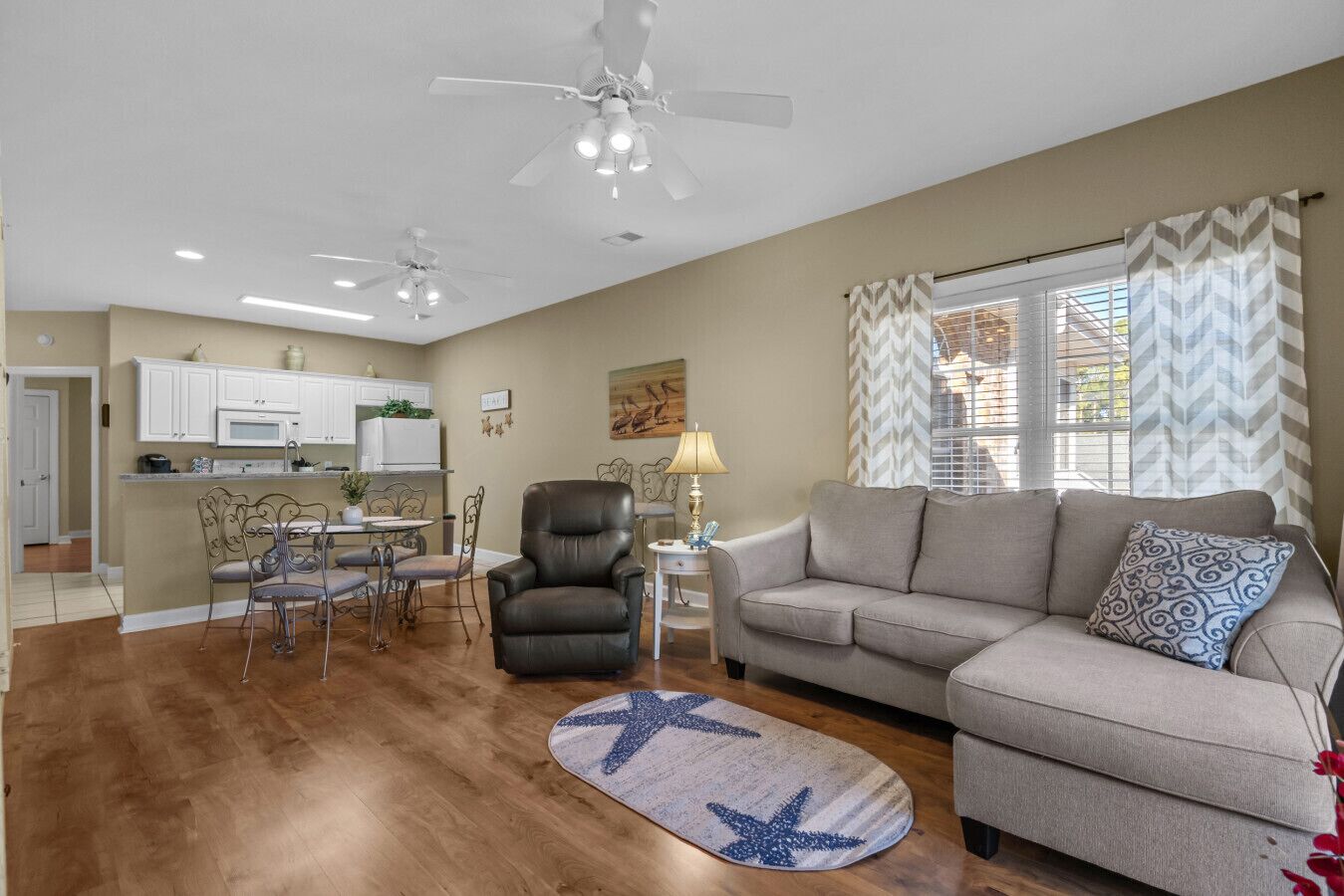 A modern living room with a sofa, a dining area with metal chairs, a black leather chair, and a star-patterned rug.