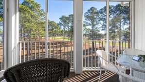 A covered outdoor area with a table and chairs, a view of a golf course, and a white railing. - Stunning Sunset Beach Getaway (Sunset Beach)