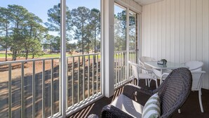A covered outdoor seating area with a table and chairs, large windows offering a view of trees and a yard. - Stunning Sunset Beach Getaway (Sunset Beach)