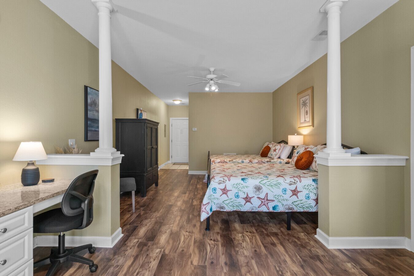 A bedroom with a bed, desk, chair, and a ceiling fan.