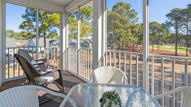 A covered porch with wicker chairs and a glass table, overlooking a residential area with houses and trees. - Stunning Sunset Beach Getaway (Sunset Beach)