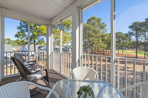 Une véranda avec des fauteuils en osier et une table en verre, donnant sur un quartier résidentiel avec des maisons et des arbres.