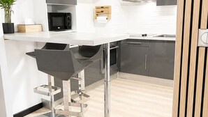 Una cucina moderna con un piano di lavoro bianco, elettrodomestici in acciaio inossidabile e uno sgabello da bar nero.
