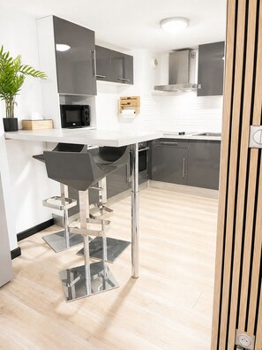A modern kitchen with a white countertop, stainless steel appliances, and a black bar stool. - LVAM - Appartement T3 - 6 personnes - Au coeur du Cap d'Agde - Piscine (Agde)