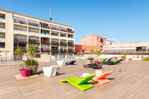 A rooftop pool area with lounge chairs, potted plants, and a building with balconies. - LVAM - Appartement T3 - 6 personnes - Au coeur du Cap d'Agde - Piscine (Agde)