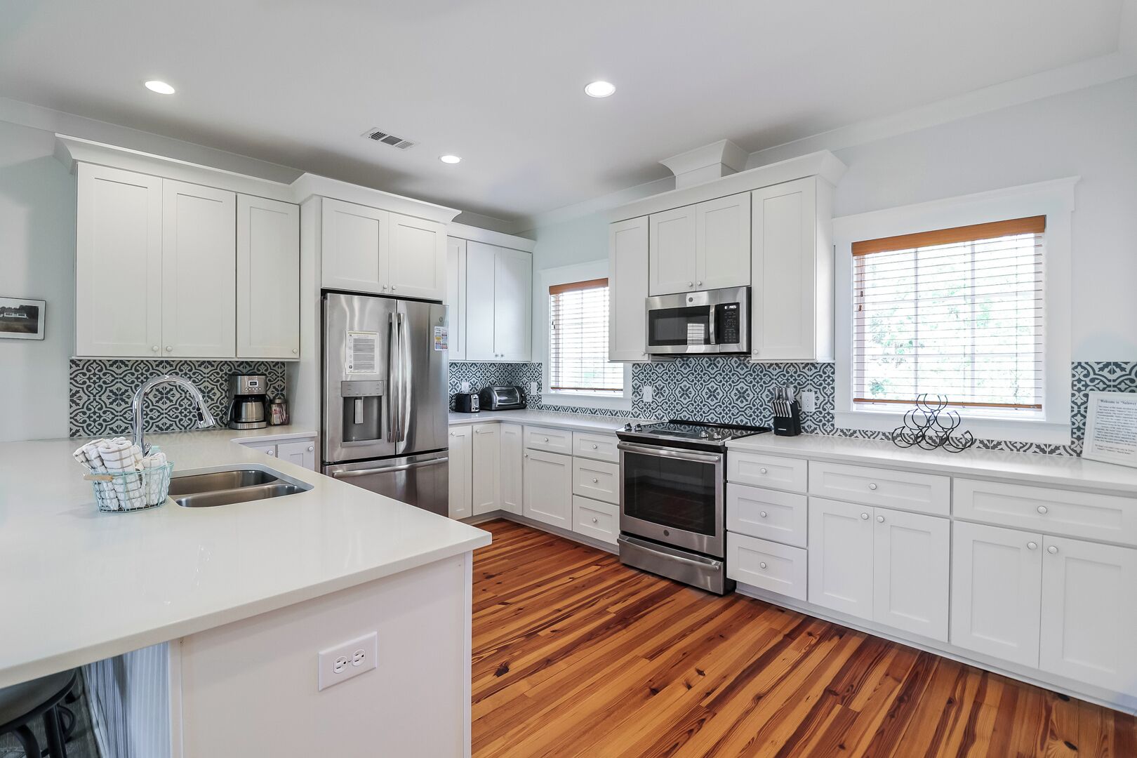 Una cucina moderna con mobili bianchi, elettrodomestici in acciaio inossidabile, pavimento in legno e piastrelle decorative a parete.