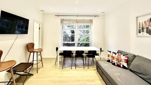 Un salon moderne comprenant un coin repas, un téléviseur à écran plat fixé au mur et une grande fenêtre laissant entrer la lumière naturelle.