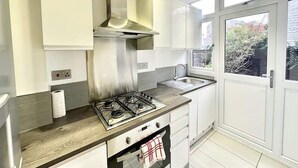 Une cuisine moderne avec des armoires blanches, une hotte en acier inoxydable, une cuisinière à gaz, un four encastré et une fenêtre donnant sur l’extérieur.