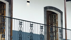 Un bâtiment avec un toit recouvert de tuiles, un balcon doté de balustrades noires décorées et un mur en briques.