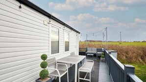 A covered outdoor area with a table and chairs, a small potted plant, and a view of a field. - Host & Stay | Long View Lodge (Felton)