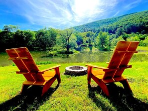 Two Adirondack chairs facing a circular fire pit with a lake and forested hills in the background. - Log Cabin with modern comfort, hiking,fishing&more (Big Indian)
