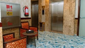 A lobby with patterned wallpaper, two elevators, a fire extinguisher, and a small table with chairs. - GOSONA LBASIKA HOTEL (Madinah)