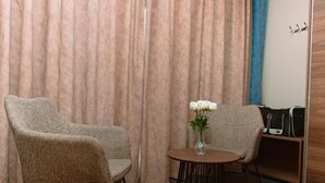 A room with two upholstered chairs, a small round table with a vase of white flowers, and a coat rack with bags. - GOSONA LBASIKA HOTEL (Madinah)