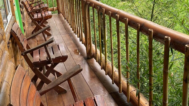 A wooden deck with benches, bamboo railings, and a view of lush greenery. - Eco Hotel Green Eden  (Pereira)