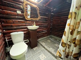 A rustic bathroom with a wooden log wall, a white sink, a toilet, and a mirror with a decorative frame.