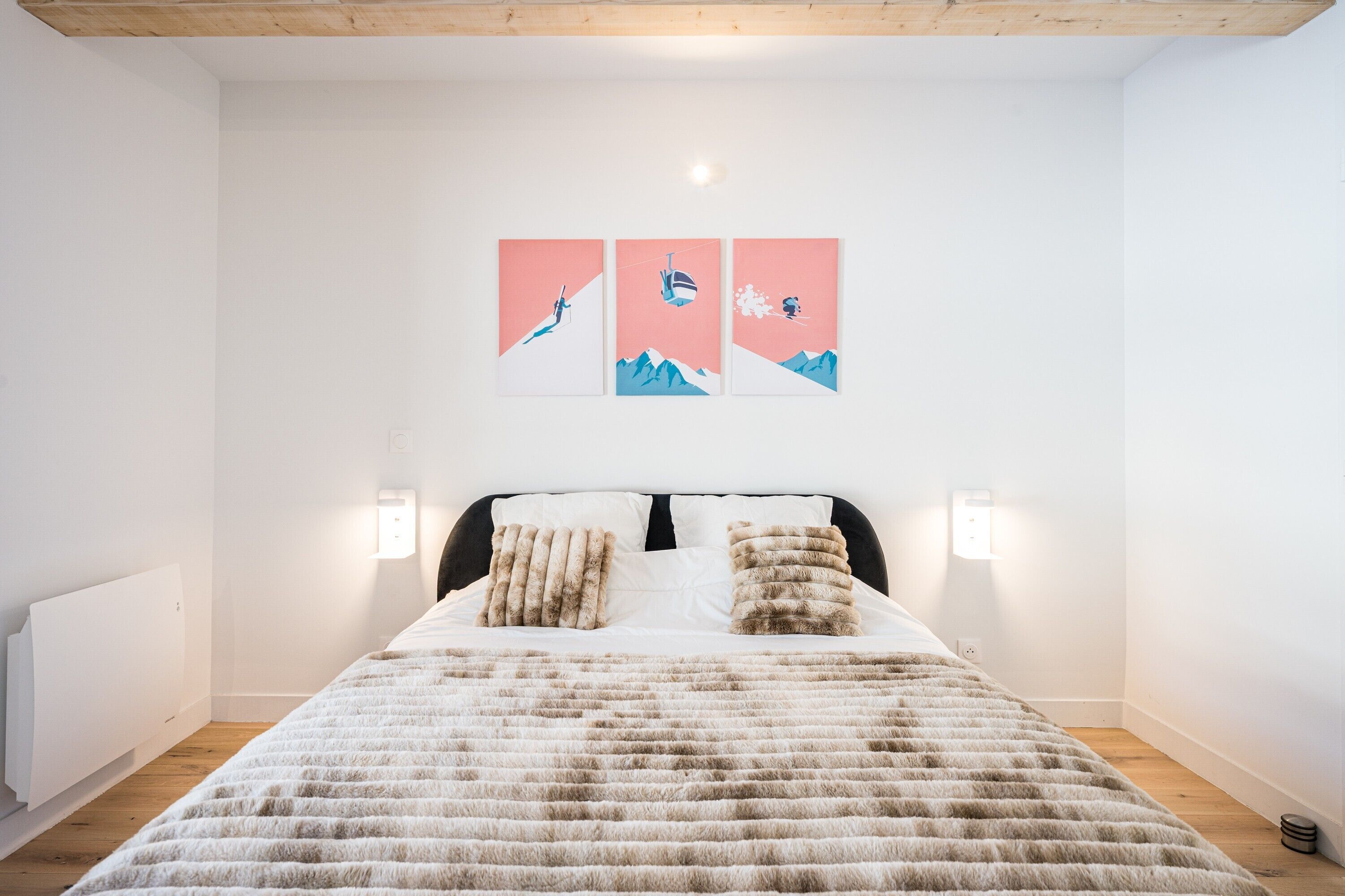 A bedroom with a bed, two wall-mounted lamps, and three wall-mounted artworks depicting mountain scenes.