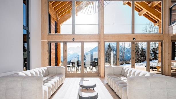 Un interior moderno con un amplio sofá, una zona de comedor y vistas a montañas a través de amplios ventanales.