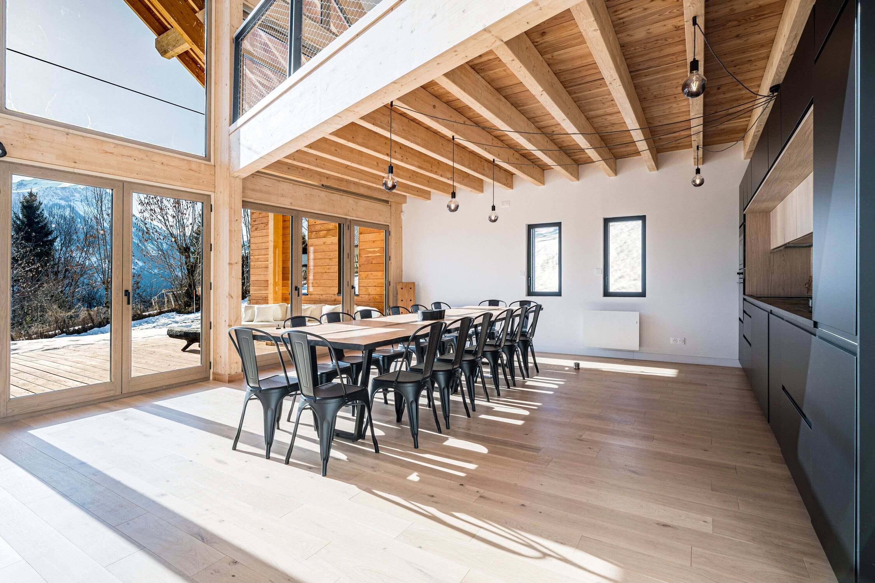 A modern kitchen with wooden beams, a dining area with chairs, and large windows.