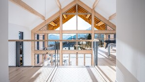 Un interior espacioso con techo alto, vigas de madera, ventanas amplias y vistas a montañas.