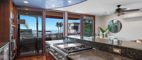A modern kitchen with a gas stove, wooden cabinets, and a view of the ocean.