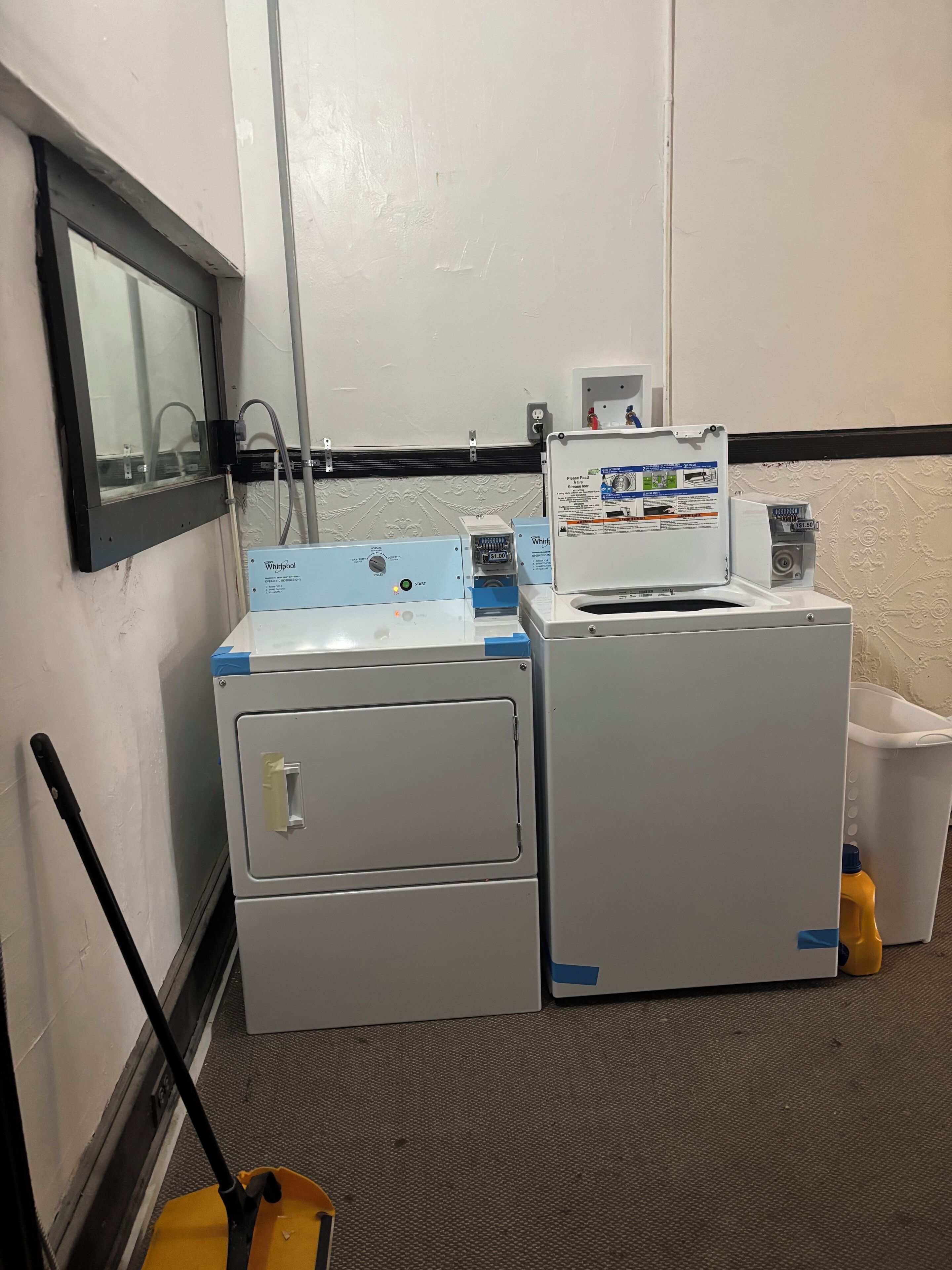 A laundry area with a Whirlpool washer and dryer, a mop, and a trash bin.