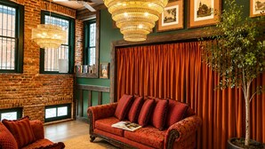 A cozy room with a brick wall, a red sofa, a chandelier, and framed pictures on the wall. - Rachael's Inner Harbor Boutique Inn (Baltimore)