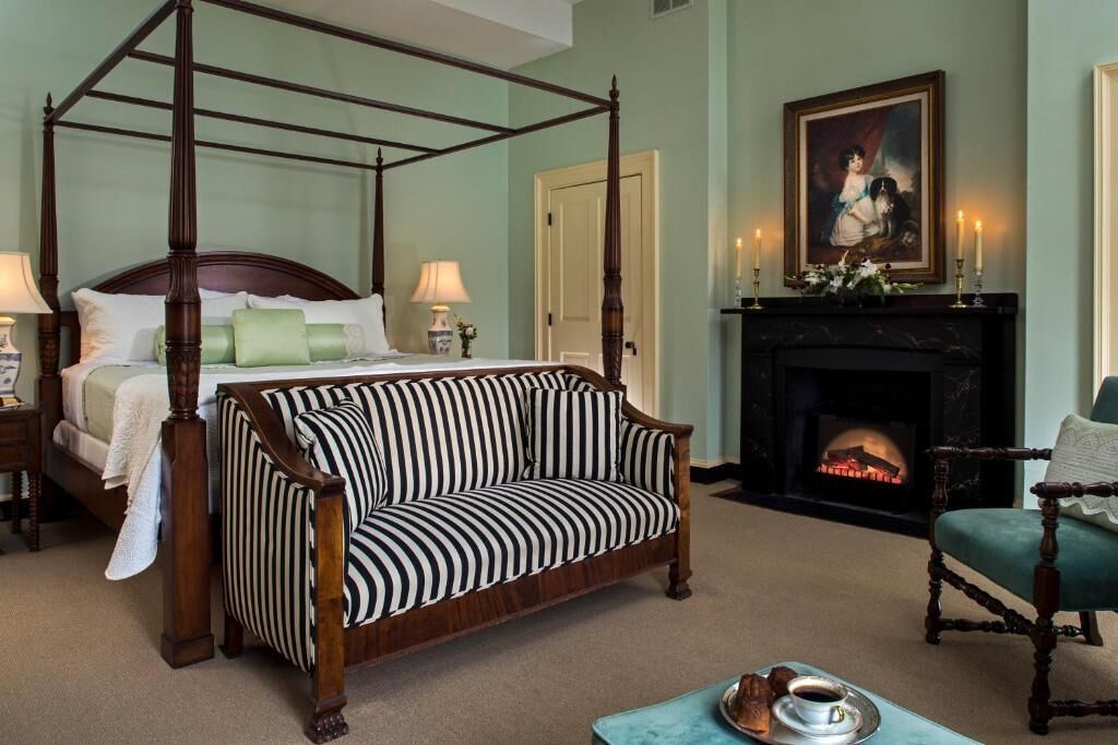 Un lit à baldaquin avec un fauteuil à revêtement vert, une cheminée et un tableau accroché au mur.