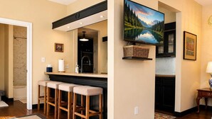 A kitchen with a bar area, wooden stools, a television, and a painting. - Rachael's Inner Harbor Boutique Inn (Baltimore)