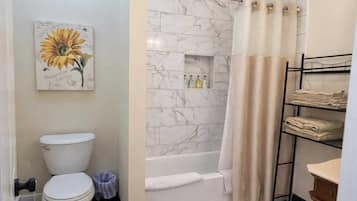 Un baño con inodoro, ducha con pared de mármol, estante con artículos de aseo y toallero.