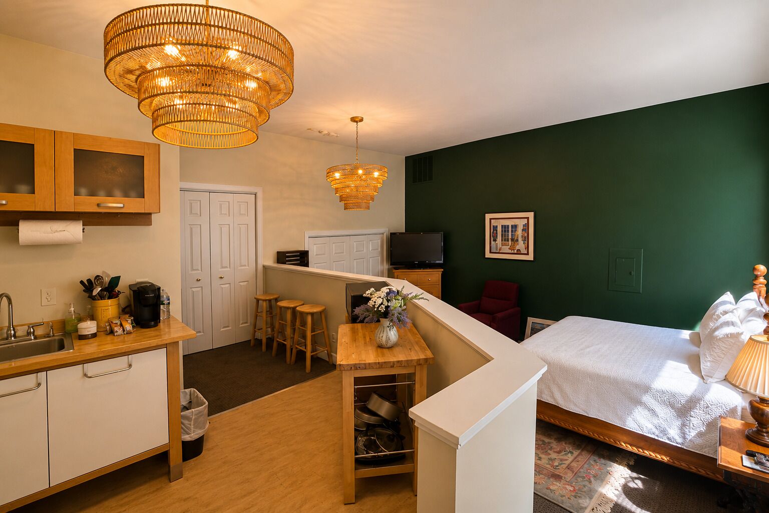 A compact hotel room with a kitchenette, a bed, a TV, and a dining area.