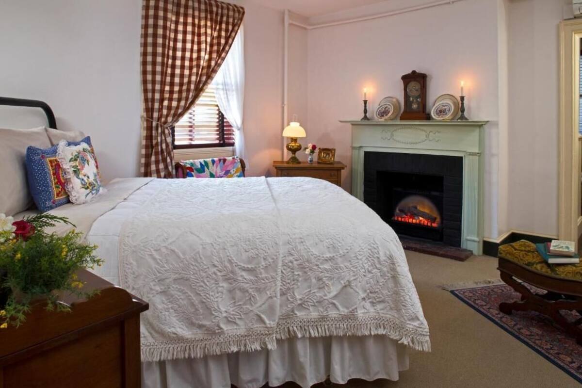 A bedroom with a bed, a nightstand, a fireplace, and a window with curtains.