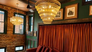 A room with a brick wall, a red sofa, a chandelier, and framed pictures on the wall. - Rachael's Inner Harbor Boutique Inn (Baltimore)