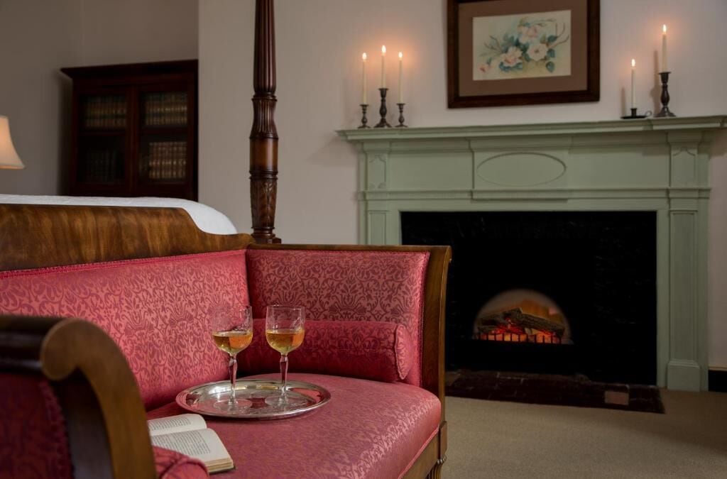 A room with a bed, a fireplace, and two glasses of wine on a tray.