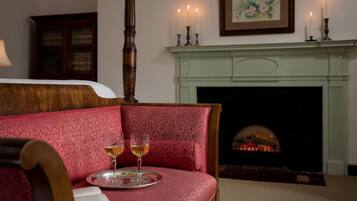 A room with a bed, a fireplace, and two glasses of wine on a tray.
