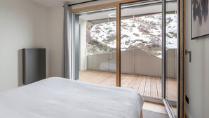 Une chambre moderne avec un grand lit et une porte-fenêtre coulissante donnant sur un balcon avec vue sur un paysage enneigé.