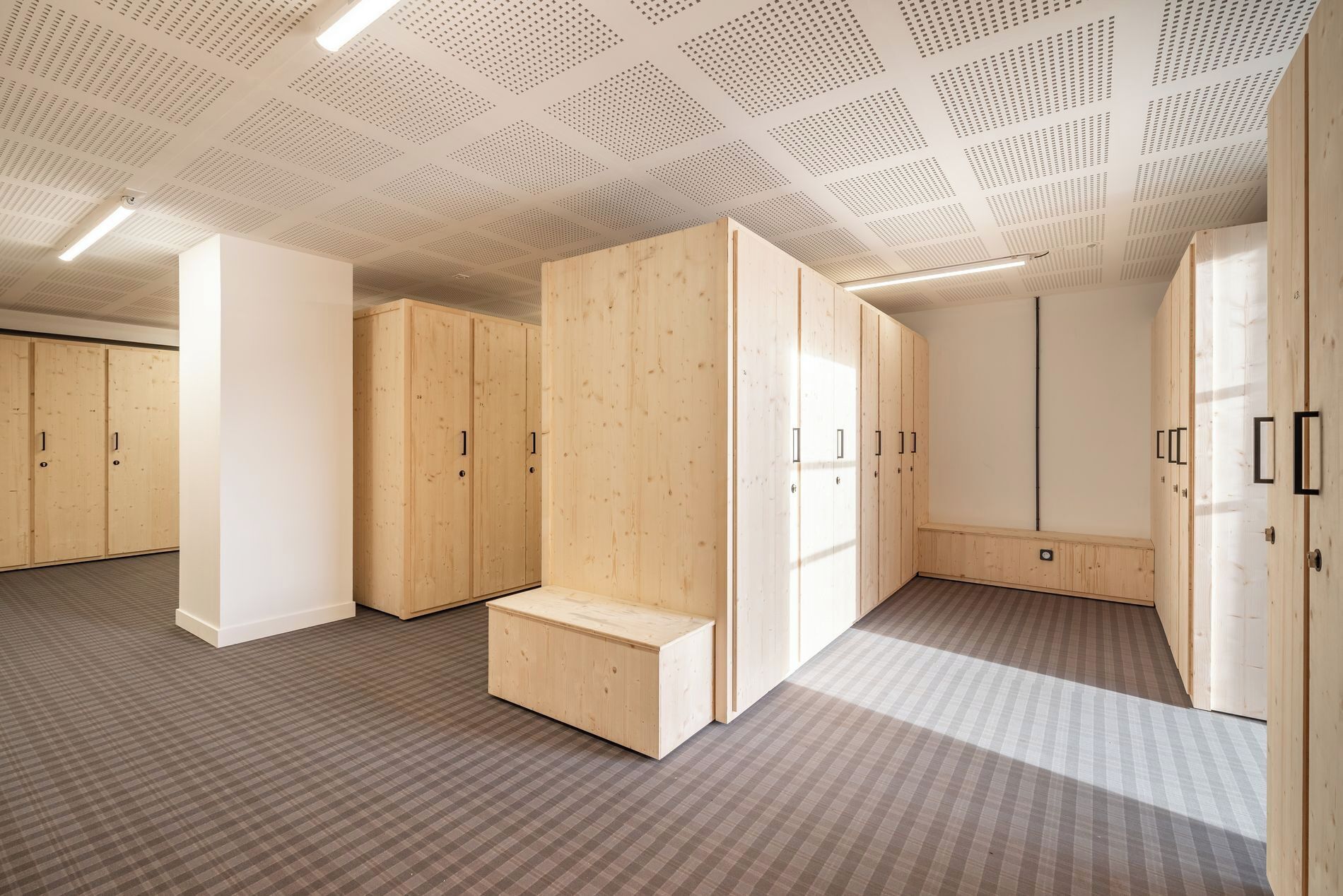 A room with wooden wardrobes, a bench, and a patterned carpet.