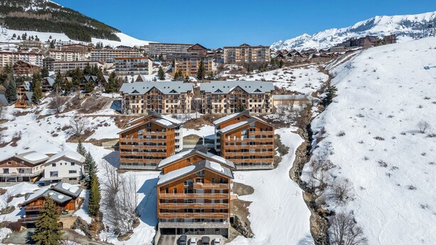 Une station de ski avec plusieurs bâtiments en bois, un paysage enneigé et un ciel dégagé.